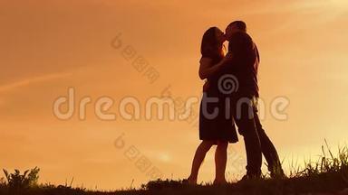 日落时分一对夫妇的剪影。 男人和女人的剪影在夕阳下缓慢的运动。 恋爱中的情侣在生活方式上接吻
